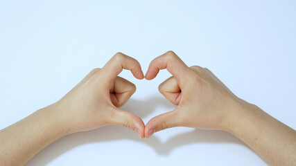 Fingers of female hands in the form of heart on white background under light.