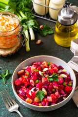 Beetroot salad vinaigrette with pickled cucumber, beans, carrots, peas, sauerkraut on a dark countertop.