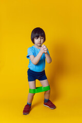 boy athlete does gymnastics with an elastic band in a sports club on a yellow background