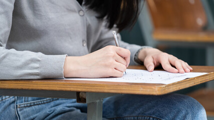 Close up of a woman student’s hand writing on notepad placed on wooden desktop