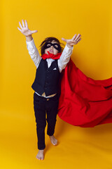 boy child super hero in a suit and black mask in the studio on a yellow background barefoot