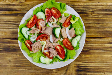 Tasty tuna salad with lettuce and fresh vegetables on wooden table. Top view