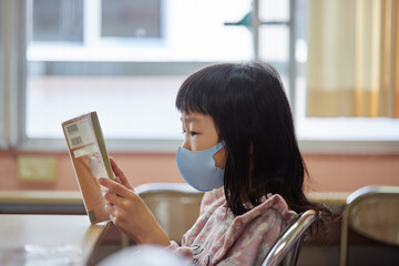 マスクを付けて図書館で読書している可愛い小学生の子供の姿