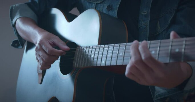 Close up of musician hand playing acoustic guitar and change chord with his fingers solo the music in dark room in slow motion shot.
