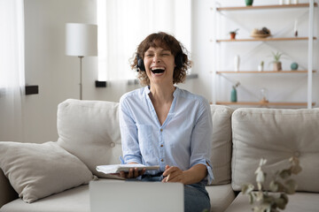 Overjoyed young Caucasian woman in earphones laugh talking on video call studying online on laptop....