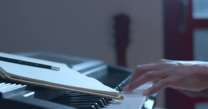 Close up on asian musician hand writing a song in notebooks and playing piano in slow motion shot.