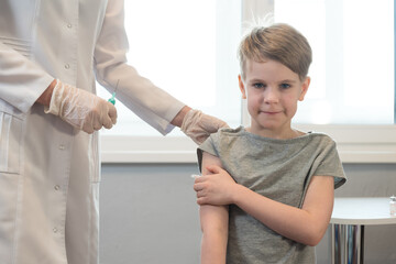 The child smiles after the injection, after the vaccination. The doctor is standing nearby, the syringe is visible. The child looks calmly at the camera and smiles