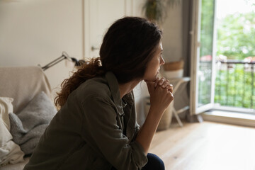 Pensive young Caucasian woman sit on sofa at home look in distance think ponder of family problem...