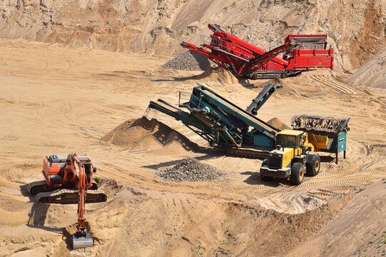 Mobile crushers and screens in open pit. Wheel front-end loader loads sand into mobile jaw crusher. Heavy machinery in the mining quarry, excavators and dump truck. Excavator on earthworks