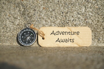 Conceptual Image: Magnetic compass with paper tag written Adventure Awaits, selective focus.