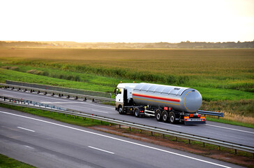 Tank truck driving on highway. Transportation of liquid goods. Metal chrome cistern tanker with...