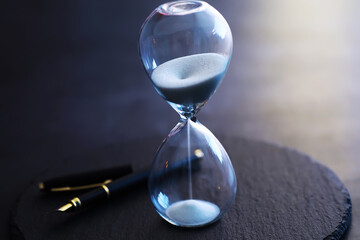 Sand running through the bulbs of an hourglass measuring the passing time in a countdown to a deadline, on a dark table background with copy space.
