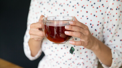 Crop close up of woman hold cup with black hot tea enjoy hygge atmosphere in own home on weekend. Female renter drink warm beverage from mug, relax in cozy house. Relaxation concept.