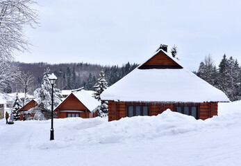 Wooden house in mountain in winter time. Log cabin in forest alone in wilderness. Wooden house with a wooden roof against background of snow-covered fir trees. Relaxation and solitude in wild