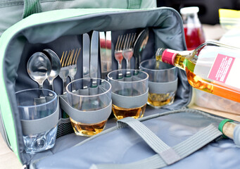 A bottle of whiskey pours alcohol into a glass in a bag. Bag with tableware to eat while traveling