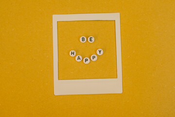Text Be Happy in a Polaroid frame on yellow background. Concept happiness, positive mindset and optimism. 