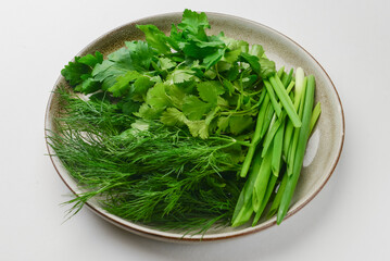 Fresh herbs - onion, dill and parsley on a plate over white background. Healthy fresh greenery,