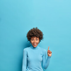 Vertical shot of positive young African American woman demonstrates advertisement above suggests...