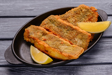 Fried fish with a piece of lemon over rustic wooden table. Delicious idea for dinner.