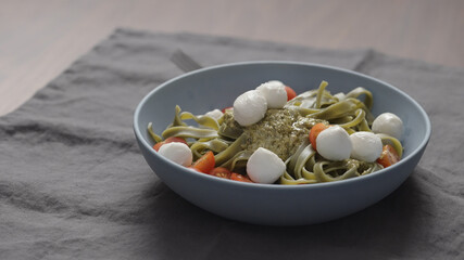 mozzarella balls to green fettuccine with pesto in blue bowl