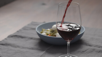 pour red wine into wineglass with bowl of fettuccine on background