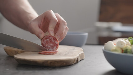 man slicing salame on olive wood board on concrete countertop