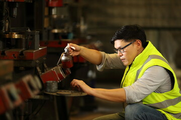 Asian engineer is lubricating the heavy machine for maintenance service inside the factory for...