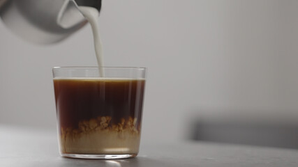 pour milk in coffee in tumbler glass on concrete countertop with copy space