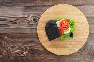Black bread sandwich on a wooden kitchen board background. Top view.