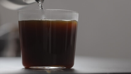 pour water in coffee in tumbler glass on concrete countertop with copy space