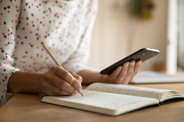 Crop close up of woman make notes handwrite in notebook using modern cellphone gadget. Female student study distant with smartphone summarize write or list in notepad. Technology concept.