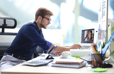 Businessman in headphones talking to his colleagues in video conference. Multiethnic business team working from office using computer PC, discussing financial report of their company.