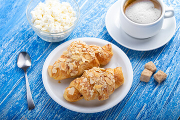 Breakfast, fresh French croissant with a cup of coffee and cottage cheese on a blue wooden table.