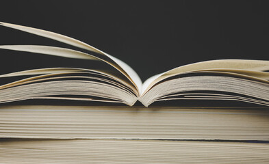 Open book on top of stack of books, on black background.