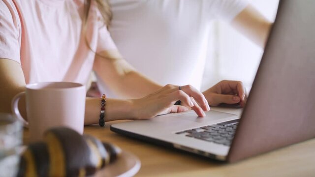 Close-up faceless young woman and man in casual clothes uses modern laptop at wooden table, couple watch screen and gesturing while do online shopping at breakfast time in modern kitchen 