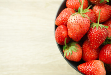 The bright red strawberries are ripe in a cup, black, placed on a wooden table, taken up close, and with a stem, green leaves, brought together.