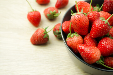 The bright red strawberries are ripe in a cup, black, placed on a wooden table, taken up close, and with a stem, green leaves, brought together.
