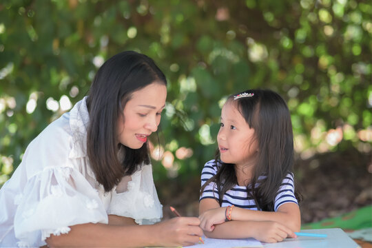 Home school concept,mother teach daughter asian children doing school homework in the home garden or park