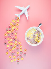 Colorful fruit corn rings with milk in the bowl, airplane on a pink background. Children's breakfast option with cornflakes.