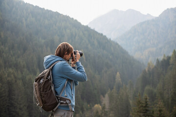 Young cheerful man photographer taking photographs with digital camera in a mountains, Travel and active lifestyle concept. - obrazy, fototapety, plakaty