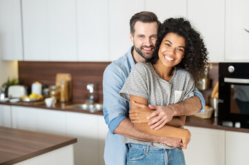 Sweet multi-ethnic couple in love stands in embraces in the kitchen. Cheerful an African woman and...