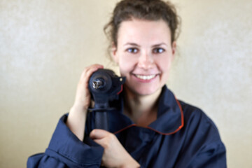 Smiling woman in workwear with a puncher near the wall.