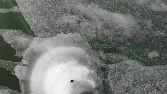 Drone video rotation over crazy patterns in ice on frozen lake with green water showing under surface