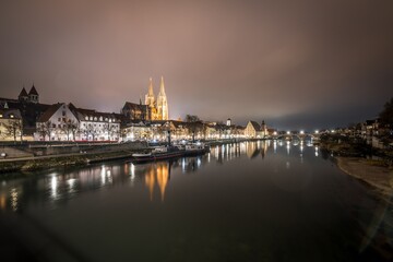 Obraz na płótnie Canvas Blick zu der steinerne Brücke in Regensburg nachts im Nebel über den Fluss Donau mit dem beleuchteten Dom und historischer Altstadt , Deutschland