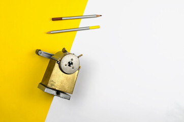 Flat lay composition with vintage pencil sharpener and two color pencils on white and yellow background.