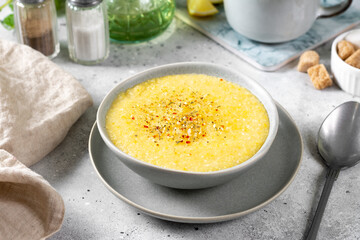 Corn porridge in a ceramic plate on the light gray kitchen table. Porridge of polenta with spices. Cream soup of polenta. Healthy Vegetarian breakfast