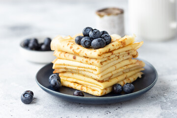 Freshly baked thin pancakes, crepes with blueberries on blue plate. Healthy breakfast. Gray background