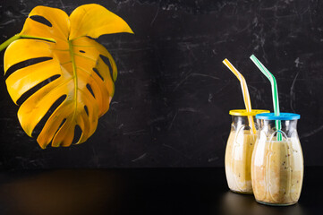Two glasses with a cocktail. Cocktails with a straw on a black background. Monstera in the...