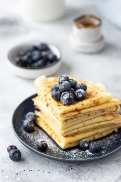 stack of thin pancakes, crepes with blueberries and powdered sugar on gray background. Delicious breakfast or dessert. vertical image