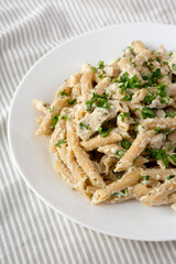 Homemade Chicken Alfredo Penne with Parsley on a white plate, side view.